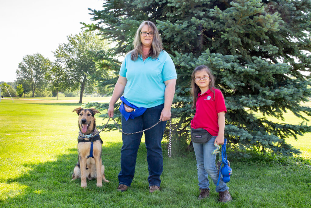 Marleila Springer standing in front of a tree with a child on one side of her and a dog on the other side of her